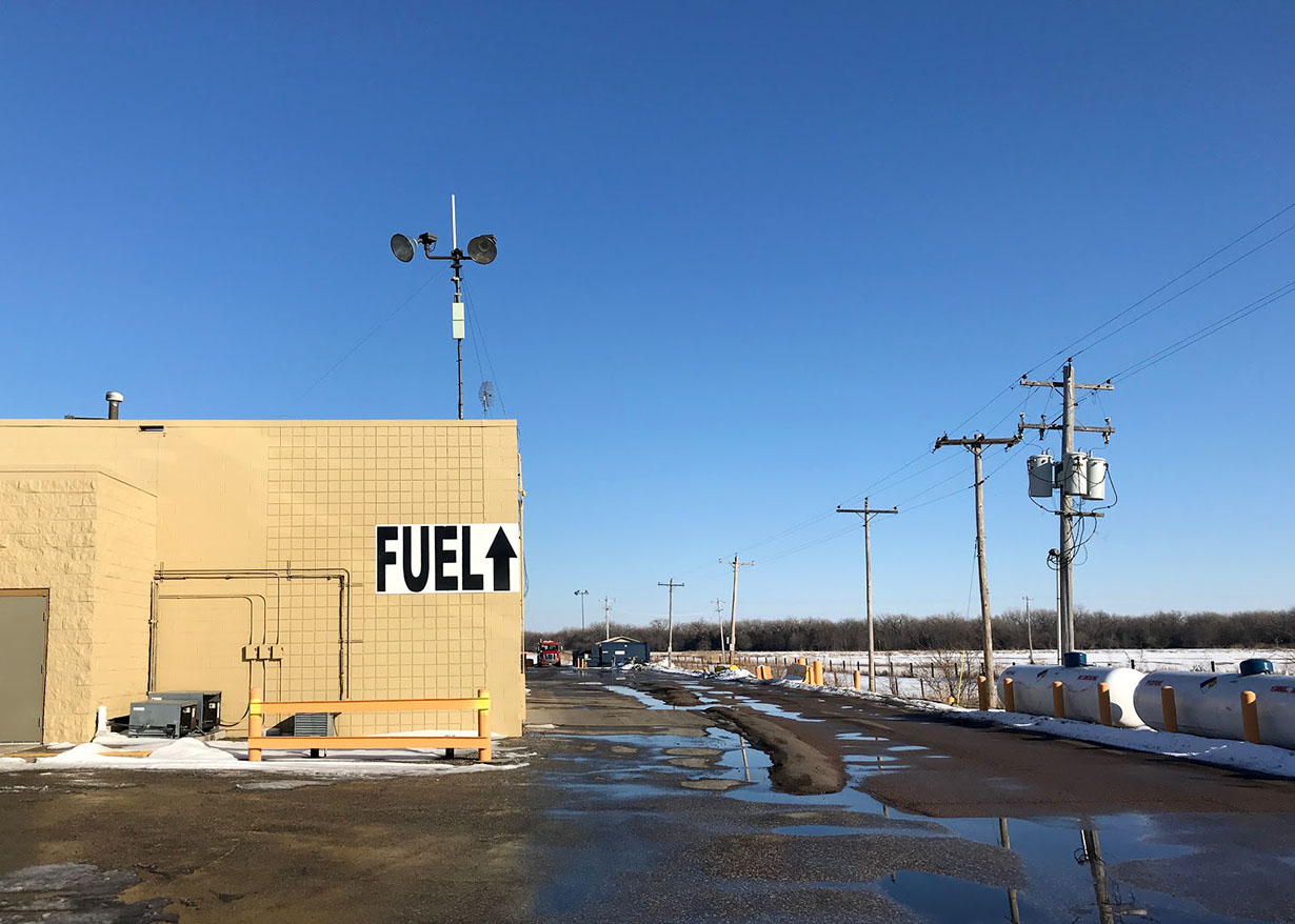 Rural landscape with “FUEL” written in big black letters on a brown building.